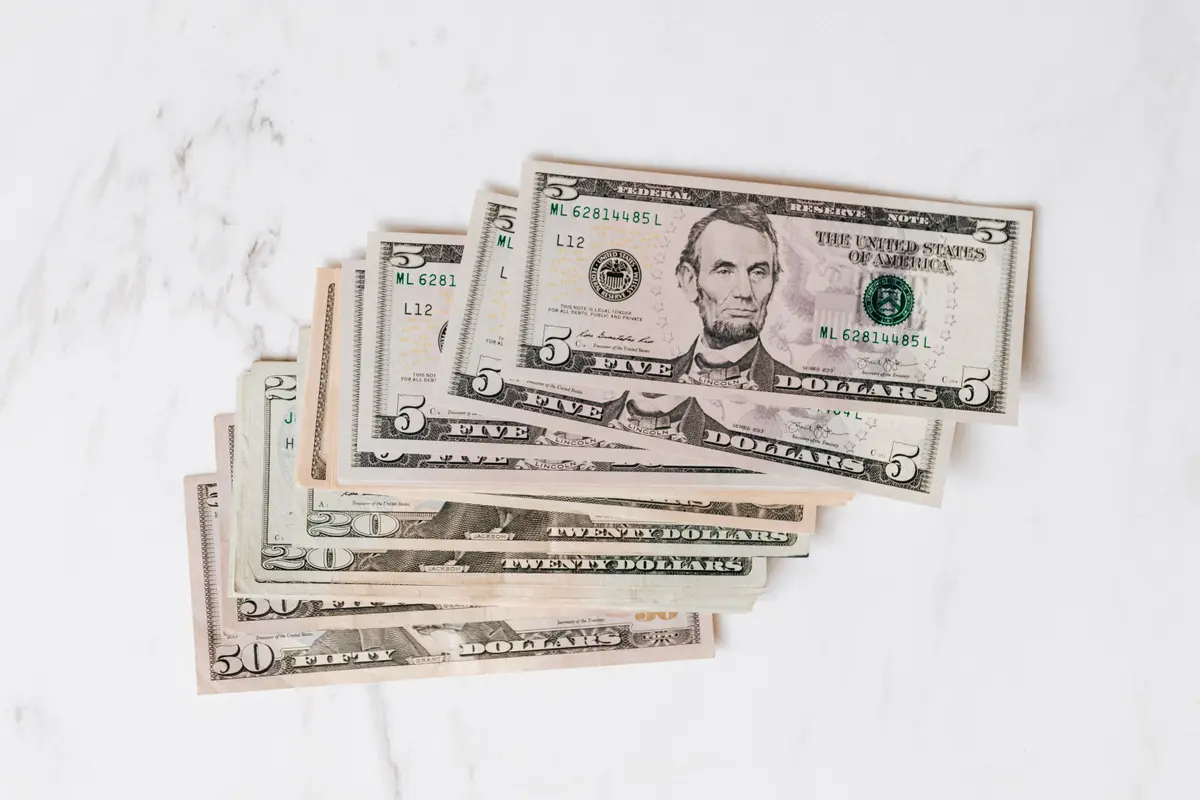 A small fan of US dollar bills on a white marble surface