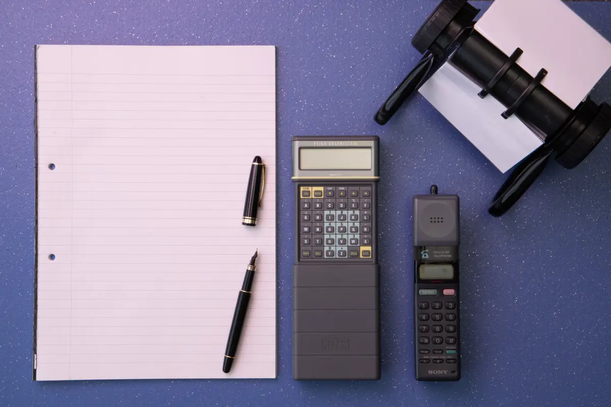 Top view of a desk with a notepad, a fountain pen, a pocket calculator and an old mobile phone