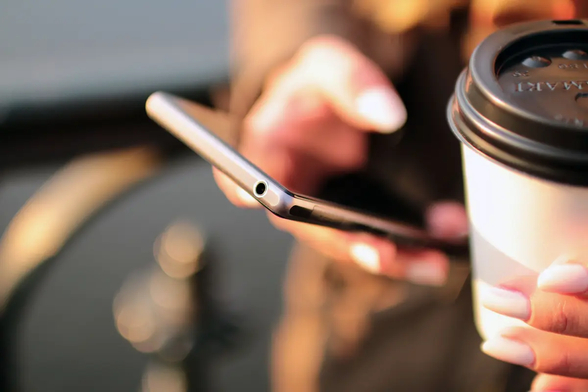 Hand holding a smartphone next to a takeaway coffee cup