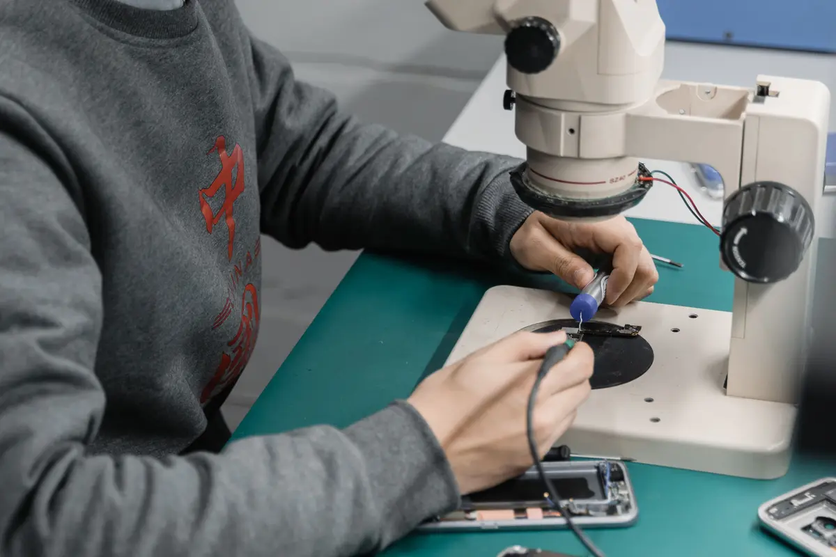 Technician working under a stereo microscope on a phone repair bench