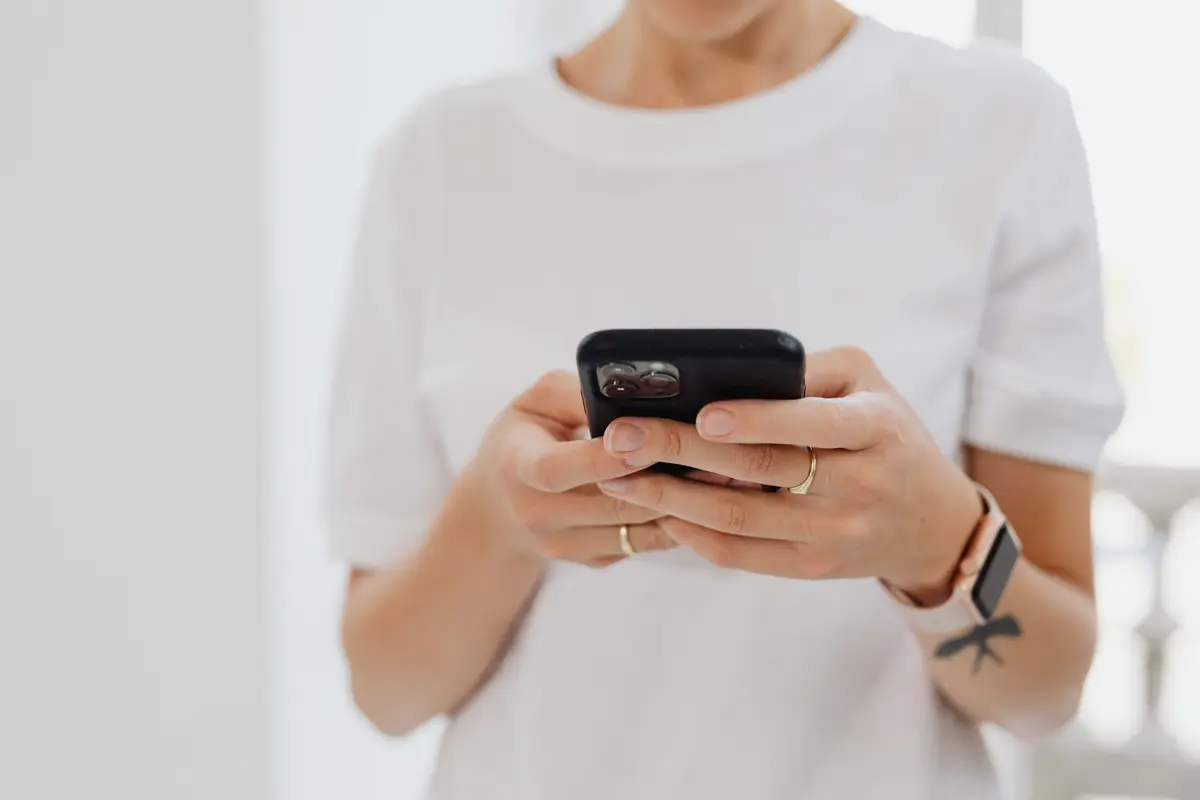 Woman in a white t-shirt typing on a phone held in both hands