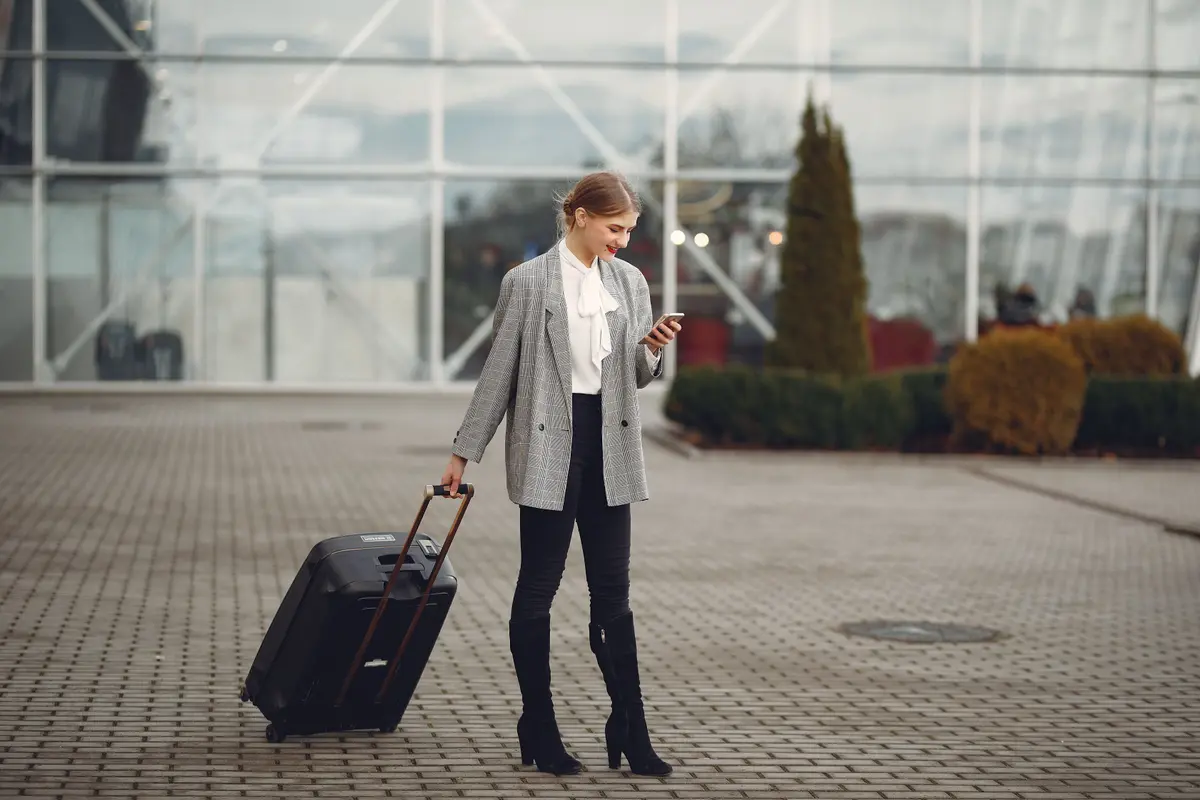 Woman pulling a suitcase outside a station while looking at her phone